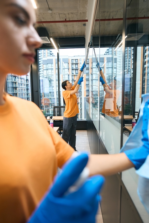 Reinigungskräfte säubern eine Glaswand in einem modernen Büro.