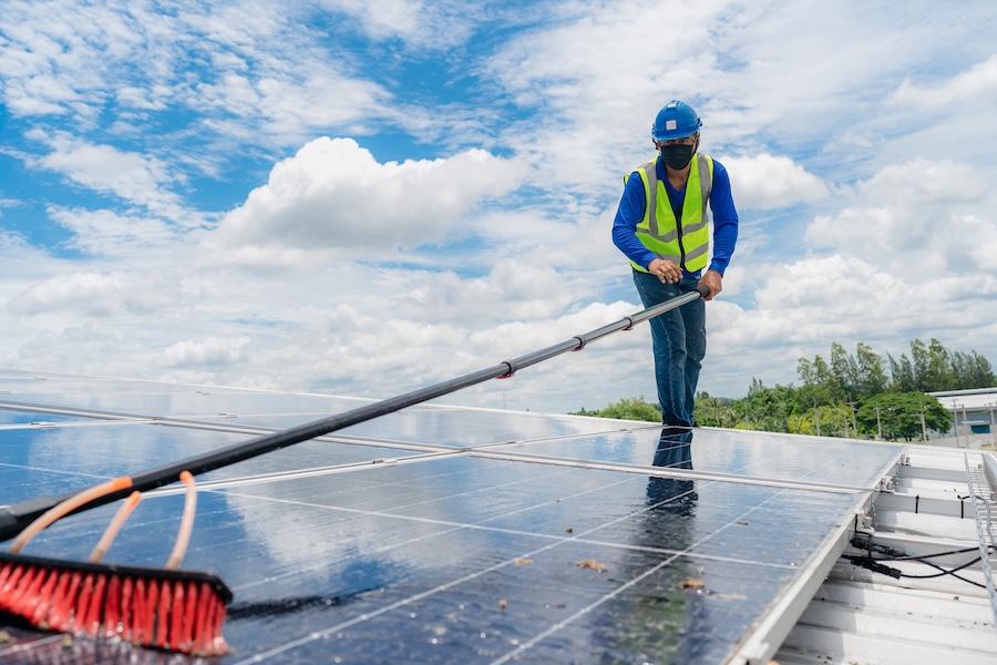 Fachkraft reinigt Photovoltaikmodule auf einem Dach mit einer Teleskopbürste.