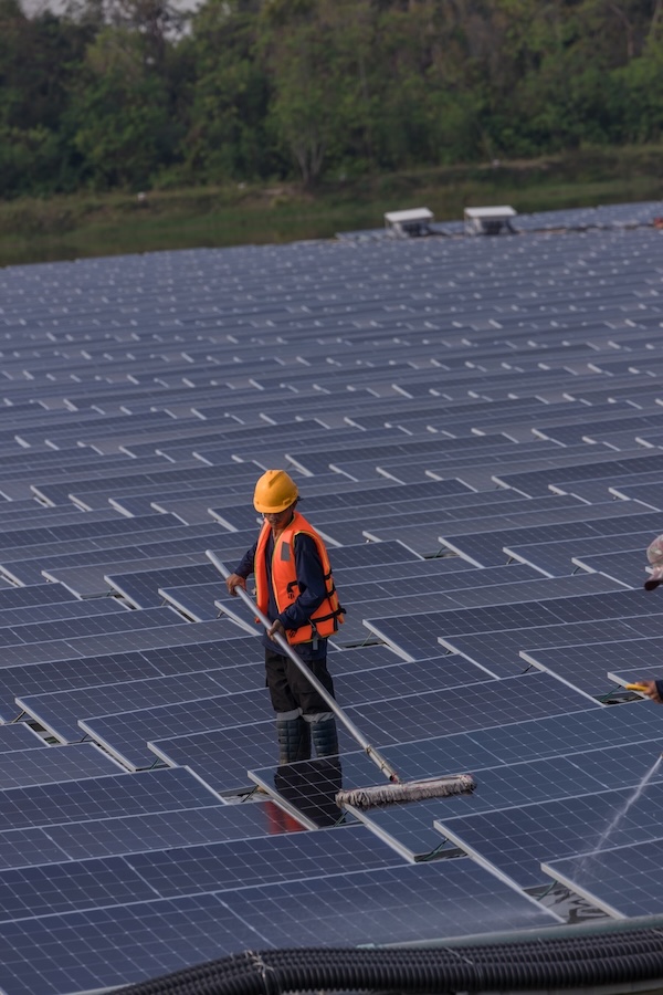 Fachkraft reinigt Solarmodule einer großen Photovoltaikanlage mit einer langen Bürste.